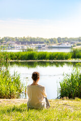 A woman is meditating, sitting in the grass in front of the river in the morning, just after sunrise. © Maxal Tamor