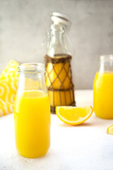 Sweet orange juice in glass decanters and a bottle stands on a white table against the background of a gray concrete wall. One bottle in ethnic style is decorated with rattan. Detox diet, vitamins. 