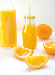 Fototapeta na wymiar Sweet orange juice in a glass bottle with a cap and a cocktail tube stands on a white background. Nearby are juicy orange slices and a decanter of juice. Detox diet drinks concept. Vertically