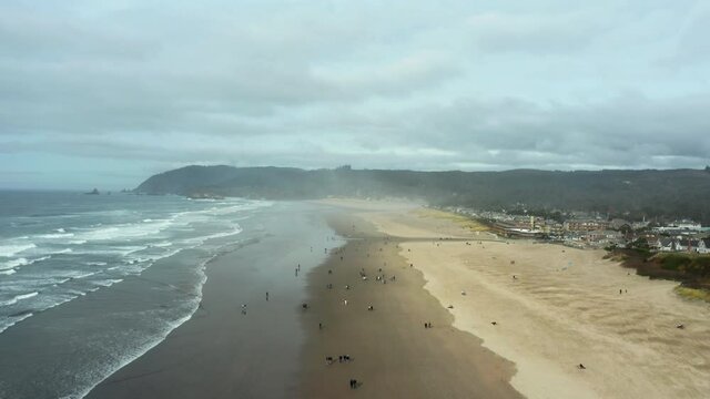 tourists at canon beach on an overcast day with mist clouds and waves
