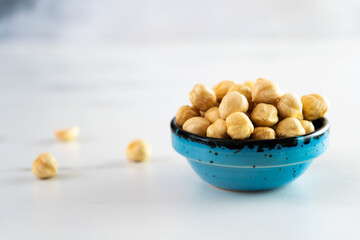 Peeled roasted hazelnuts in a blue round ceramic bowl stands on a white plate. Healthy and wholesome food high in protein, omega-3, antioxidants, minerals and vitamins. Close-up