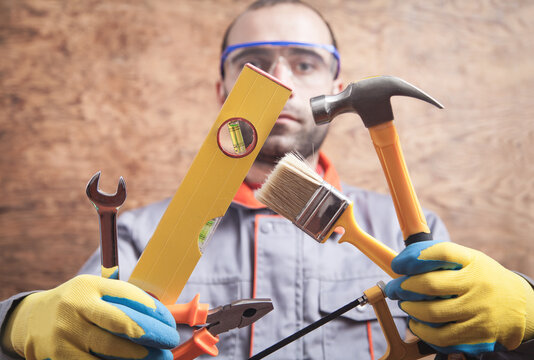 Worker holding hammer, saw, brush, level, wrench, pliers. Working tools