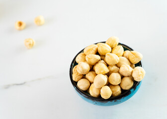 Hazelnuts in a blue bowl stands on a white plate. Delicious peeled hazelnuts. Healthy food, healthy snacks. Eating a handful of nuts a day can prevent various diseases. Top view, close-up