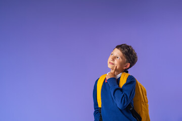 pensive schoolboy with a backpack stands and thinks on a blue background