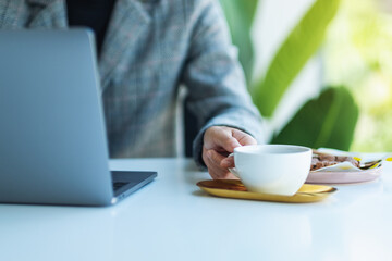 Closeup image of a business woman using and working on laptop computer while drinking coffee in office