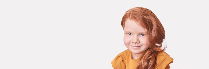 Red hair. Girl head portrait. Attractive little woman. Horizontal banner with copyspace. Sweet smile. Female child model. Funny young person. Positive expression. Looking at camera. Studio shot