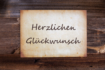 Obraz premium Old Grungy Paper With German Text Herzlichen Glueckwunsch Means Congratulations. Wooden Background