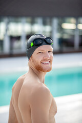 Joyful young man in swimming cap looking halfway