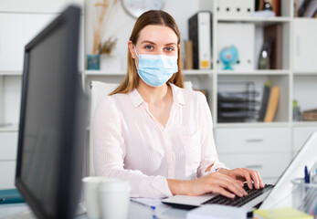 Fototapeta na wymiar Businesswoman in protective medical mask is working with project behind laptop in the office