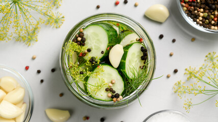 Healthy probiotic vegan food. Homemade fermented cucumbers with garlic, dill and pepper in a glass jar. Light gray background. Top view, close-up.
