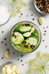 Healthy probiotic food. Homemade fermented cucumbers with garlic, dill and pepper in a glass jar. Light gray background. Top view, close-up, vertical orientation.