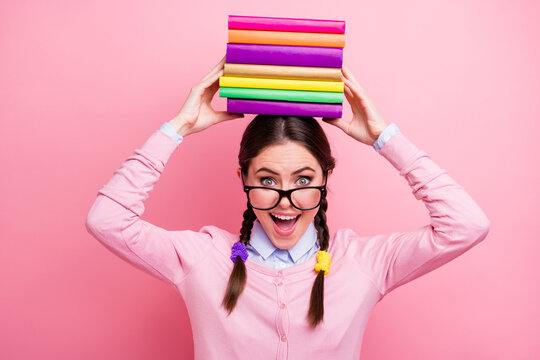 Close-up portrait of her she nice attractive pretty lovely overwhelmed cheerful cheery glad brown-haired teenage girl holding pile book on head isolated over pink pastel color background