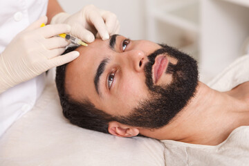 Fototapeta na wymiar Bearded man getting face filler injections by cosmetologist