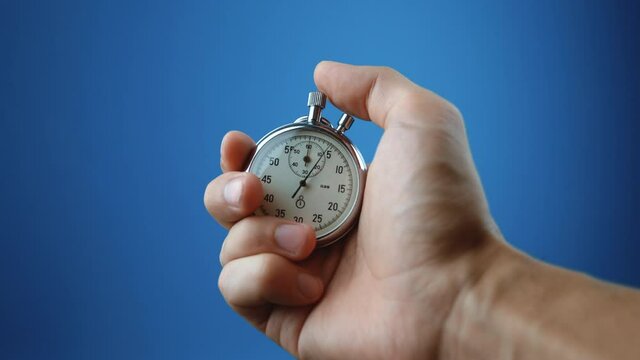 Male hand holding analogue stopwatch on blue color background. Time start with old chronometer man presses start button in the sport concept. Time management concept.
