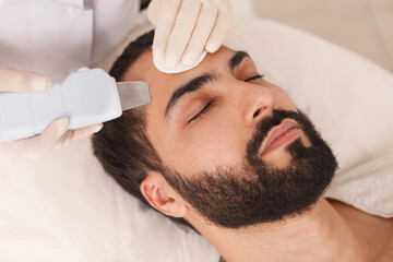 Fototapeta na wymiar Close up of a handsome bearded man getting ultrasound cleanse by cosmetologist