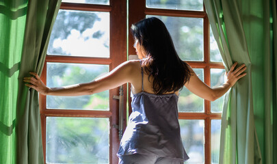 young woman in modern apartment opening window curtains after wake up