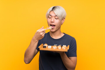 Young asian man with sushi over isolated yellow background © luismolinero