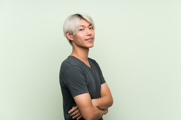 Young asian man over isolated green background with arms crossed and looking forward