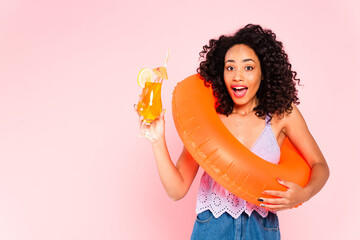 excited african american woman standing with swim ring and holding cocktail isolated on pink