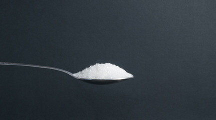 a teaspoon of white granulated sugar on a black background, a source of glucose and sucrose, an...