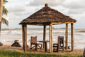Africa empty beach with bamboo chairs and thatched roof as protection from rain and sun, the plate is Axim Ghana West Africa