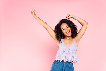 excited african american woman with hands above head on pink