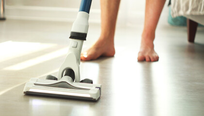 Man cleaning floor with cordless vacuum cleaner in the modern white living room. Concept of easy cleaning with a wireless vacuum cleaner.