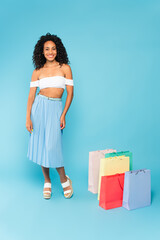 happy african american girl standing near shopping bags on blue