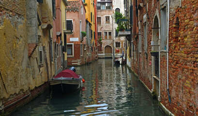 Fototapeta na wymiar Quiet Canal in Venice with boats and crumbling walls.