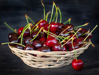 a wicker plate of vines full of ripe cherries on a black background of wood surface
