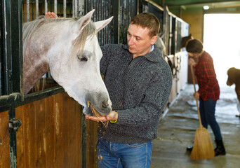 Portrait of positive man in casual clothes who works at horse stable