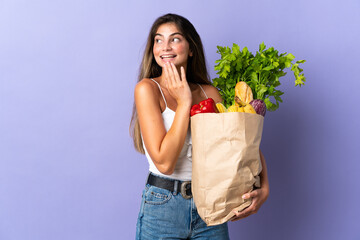 Young woman holding a grocery shopping bag looking up while smiling