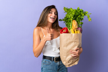 Young woman holding a grocery shopping bag giving a thumbs up gesture