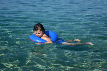 Little boy with inflatable ring swimming in the sea. Child with a floating ring enjoy in crystal clear water