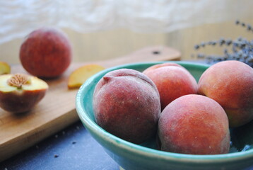 Fresh peaches in a handmade ceramic bowl served on the table. Wooden cutting board with sliced peach in the background.