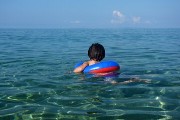 Little boy with inflatable ring swimming in the sea. Child with a floating ring enjoy in crystal clear water