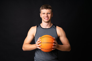 Handsome young man playing basketball over isolated black wall