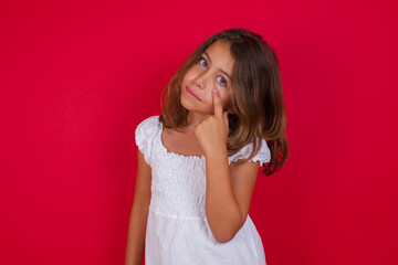 Little caucasian girl with blue eyes wearing white dress standing over isolated red background Pointing to the eye watching you gesture, suspicious expression.