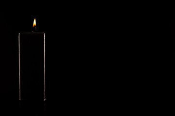 Burning black candle on dark
