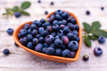 Ripe blueberries in a heart-shaped bowl on a wooden background.