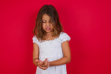 Little caucasian girl with blue eyes wearing white dress standing over isolated red background...
