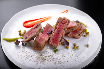 Filet mignon with capers, on a white plate, on a dark background