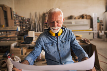 Senior carpenter sitting and looking at the blueprint paper