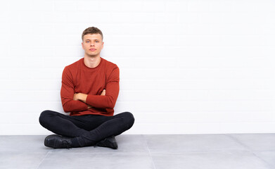 Young handsome man sitting on the floor keeping arms crossed