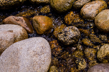 Fototapeta na wymiar Close up brown natural wet rocks in the stream. Water flow naturally through the national park southern of Thailand.