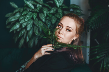 girl with green eyes and blond hair close-up with ferns in the face on a background of green leaves