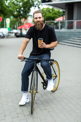 Handsome bearded man is drinking coffee and smiling while riding bicycle in street city
