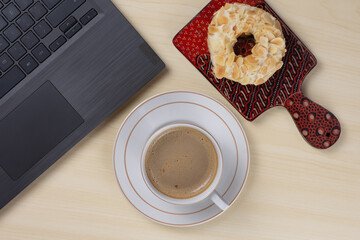 Flat-lay picture of cappuccino coffee, donut, and laptop on the desk, the concept of working from home.