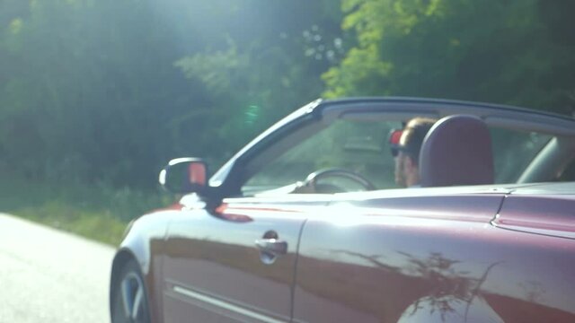 The man is riding in a convertible. Beautiful red cabriolet car driving