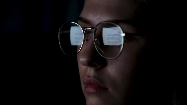 Beautiful girl works on internet with the reflection of a monitor inside glasses. Concept. Close up of woman face wearing glasses with the screen reflected in lenses isolated on black background.